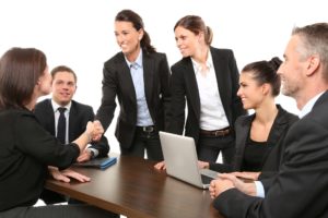 a business meeting with the group smiling and shaking hands in suits.